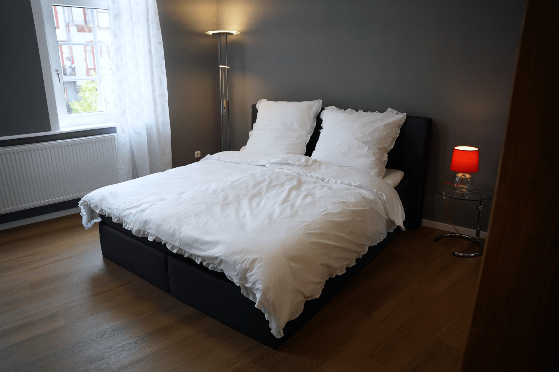 Ein Bett mit weißen Laken und Kissen in einem Schlafzimmer mit einer Lampe.