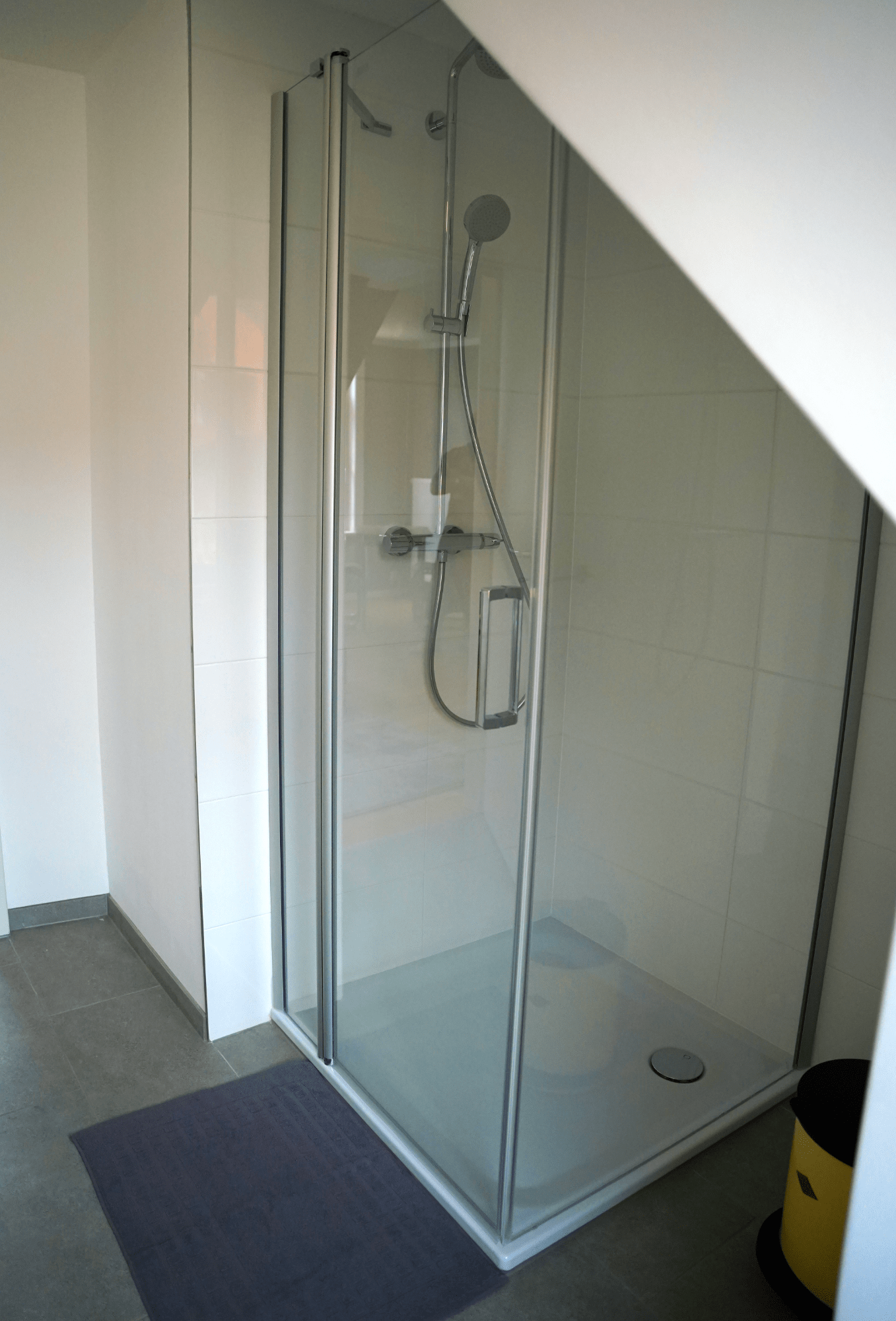 Ein Badezimmer mit Duschkabine unter einer Treppe.