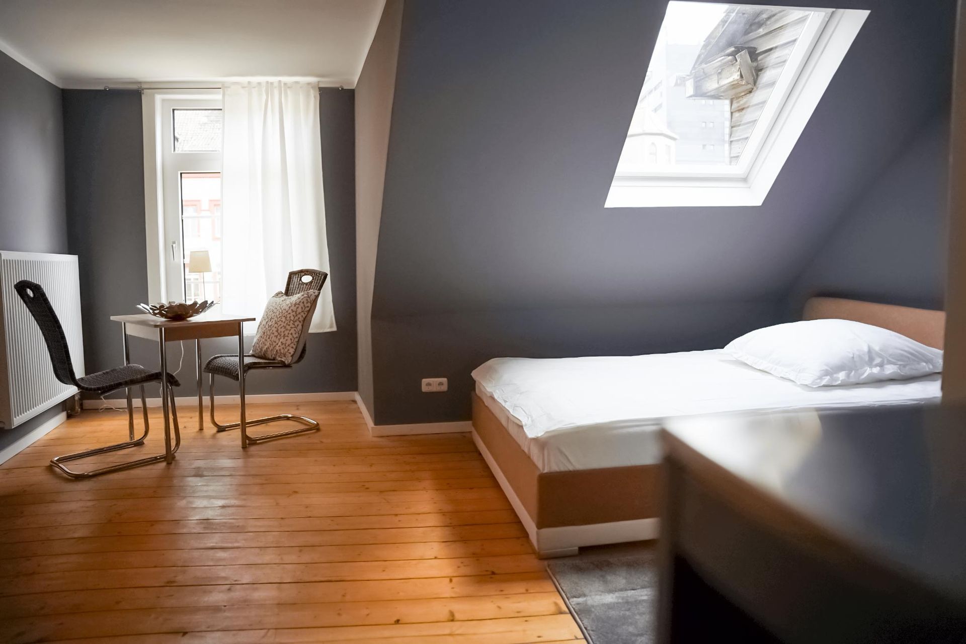 Ein Schlafzimmer mit Bett, Tisch, Stühlen und Oberlicht.