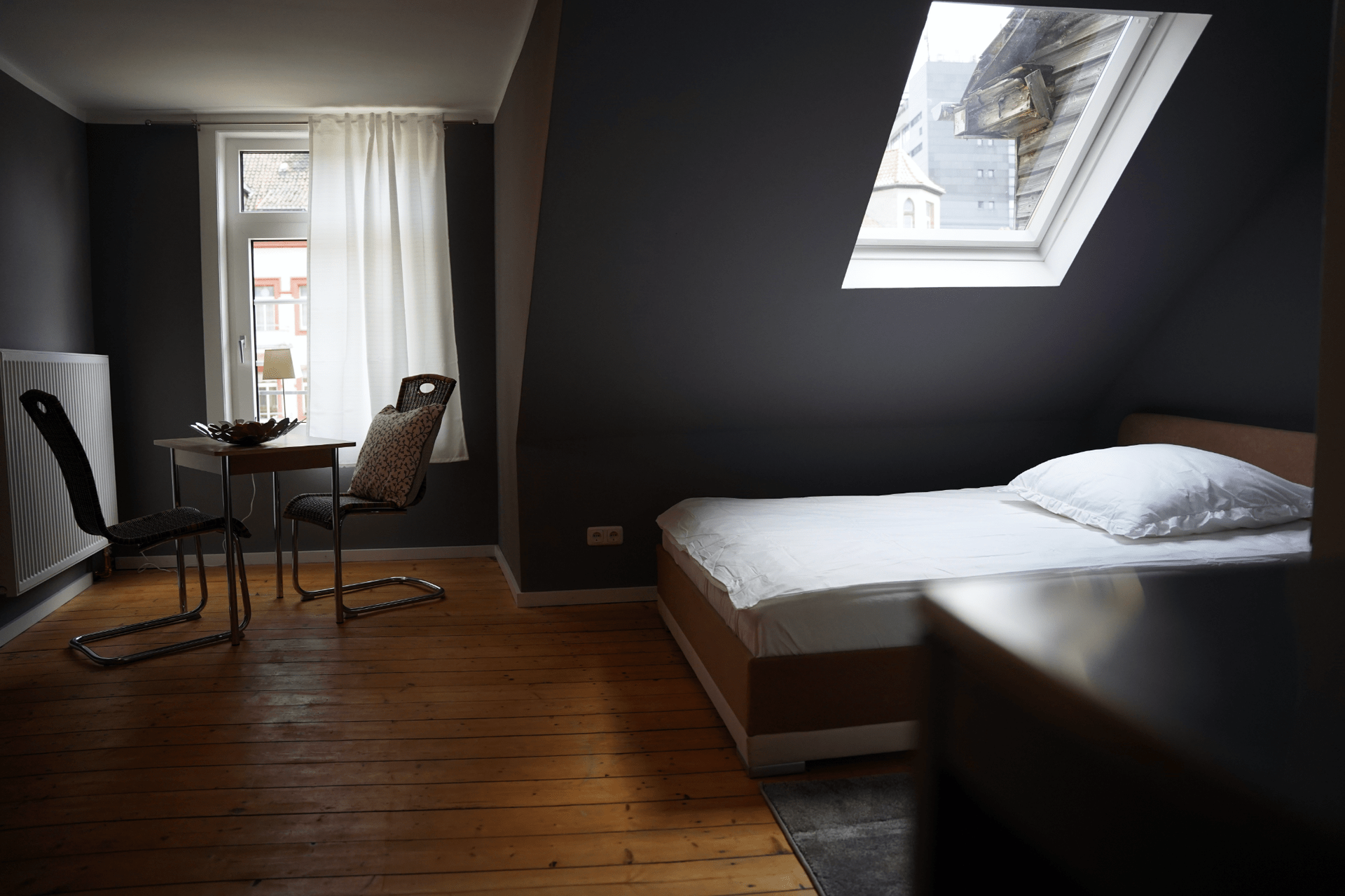 Ein Schlafzimmer mit Bett, Tisch, Stühlen und Oberlicht.