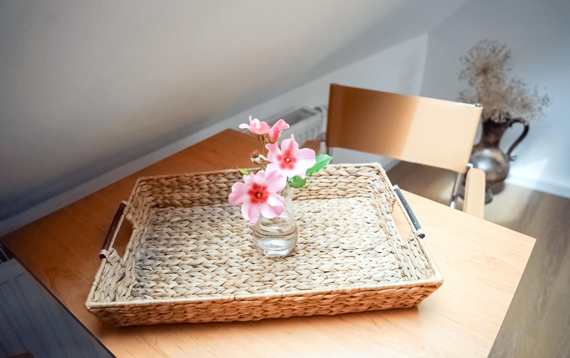 Ein Korbtablett mit einer Vase mit rosa Blumen darauf