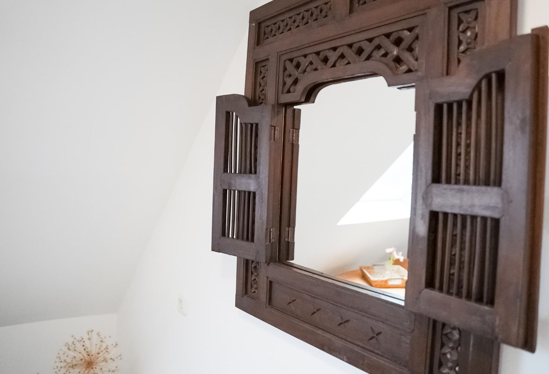 An einer Wand hängt ein großer Spiegel mit Fensterläden.