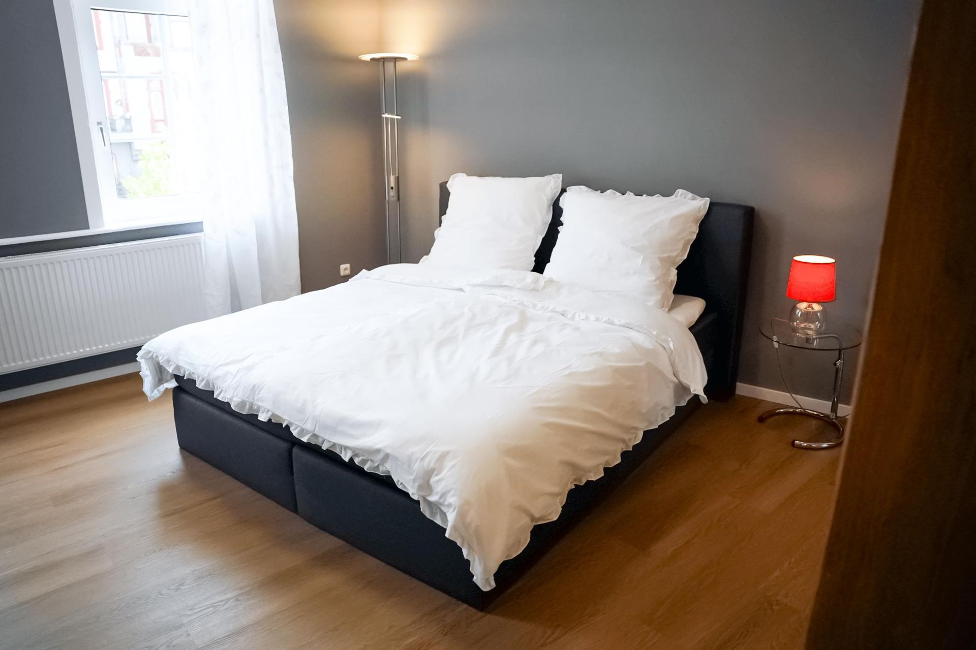 Ein Bett mit weißen Laken und Kissen in einem Schlafzimmer mit einer Lampe.