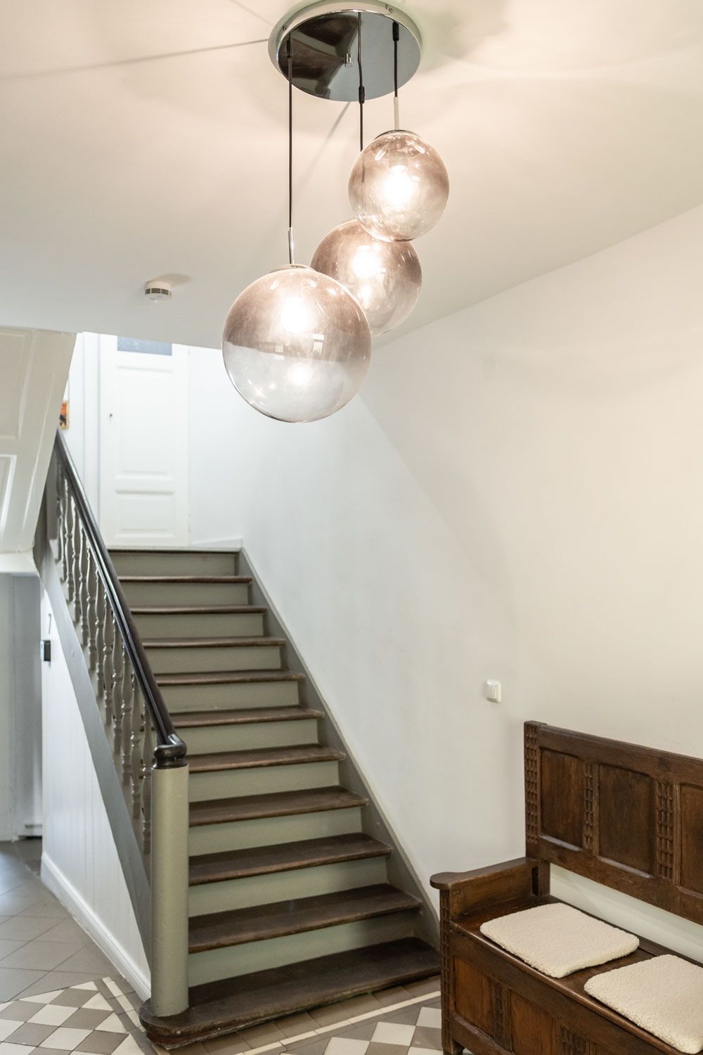 Eine Treppe mit drei Lichtern, die in einem Flur von der Decke hängen.