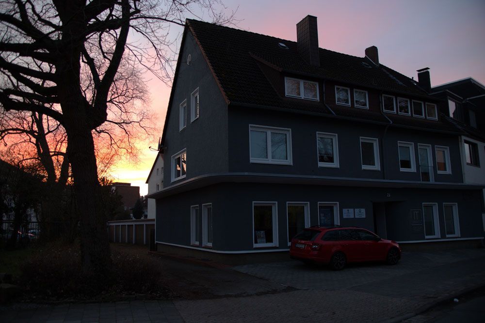 Ein Gebäude mit einem davor geparkten roten Auto bei Sonnenuntergang
