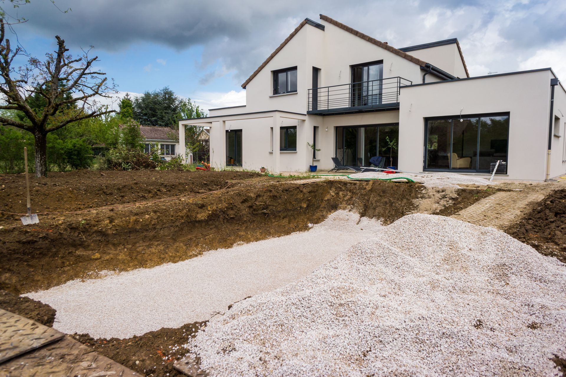 Maison blanche moderne avec allée de gravier et jardin nu sous un ciel nuageux