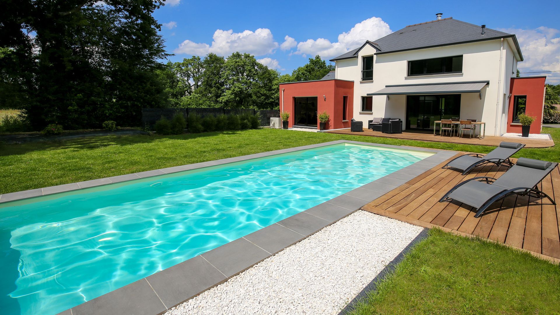 Maison moderne avec une longue piscine turquoise, une terrasse blanche et des chaises longues par une journée ensoleillée