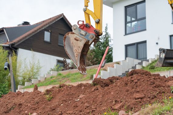 Godet d'une excavatrice creusant le sol près d'une maison et d'un escalier sur un chantier de construction