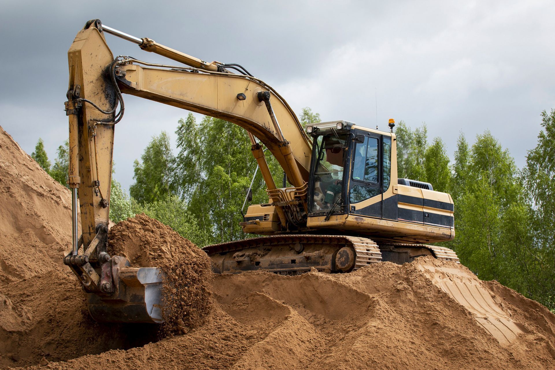 Une pelleteuse jaune creuse sur un tas de sable sur un chantier de construction, sous un ciel couvert.