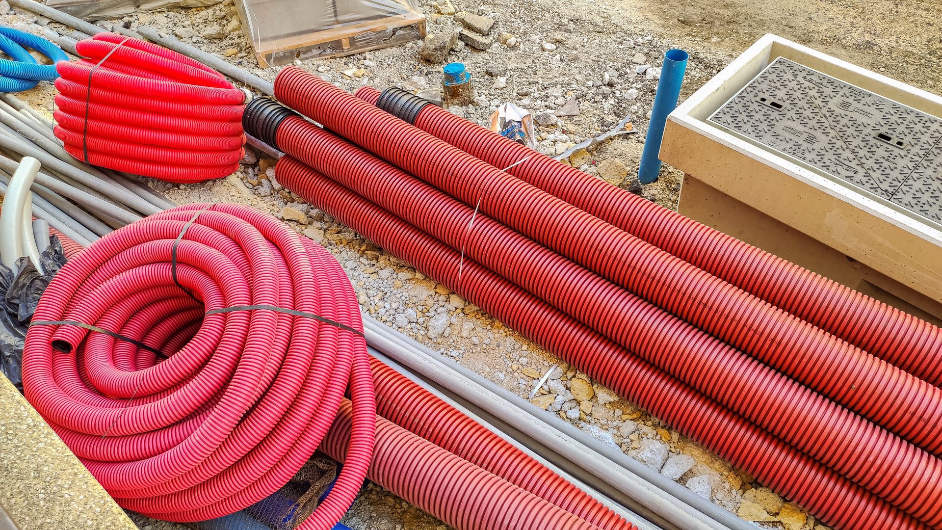 Des tuyaux de drainage rouges ondulés, enroulés et regroupés en faisceaux, sont empilés sur un chantier de construction.