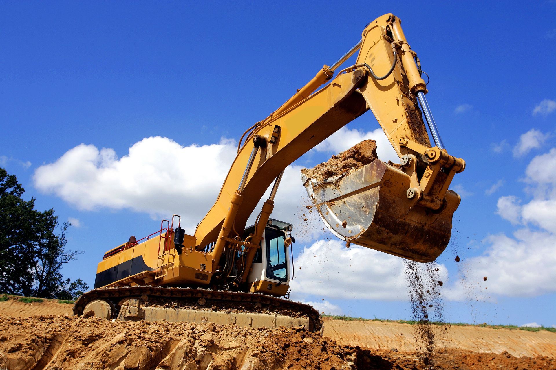 Une pelleteuse jaune déverse de la terre sur un chantier de construction sous un ciel bleu.