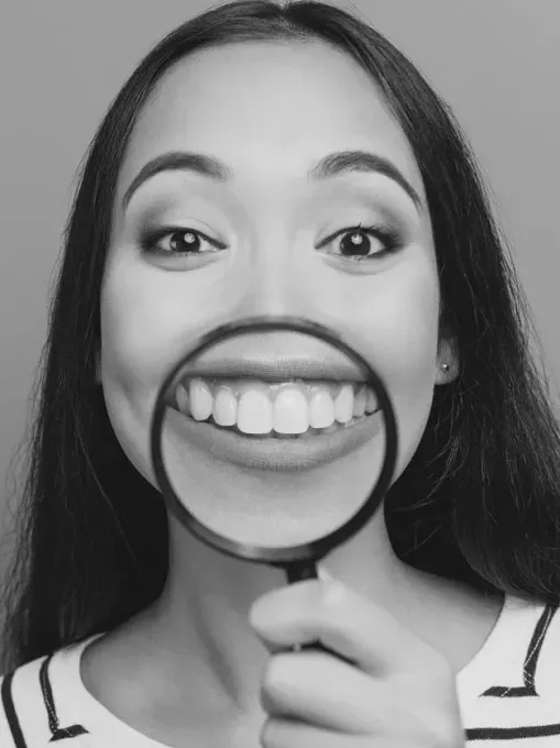 Una mujer mira sus dientes a través de una lupa.