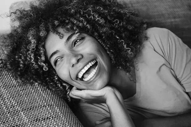 Una mujer con cabello rizado está acostada en un sofá y sonriendo.