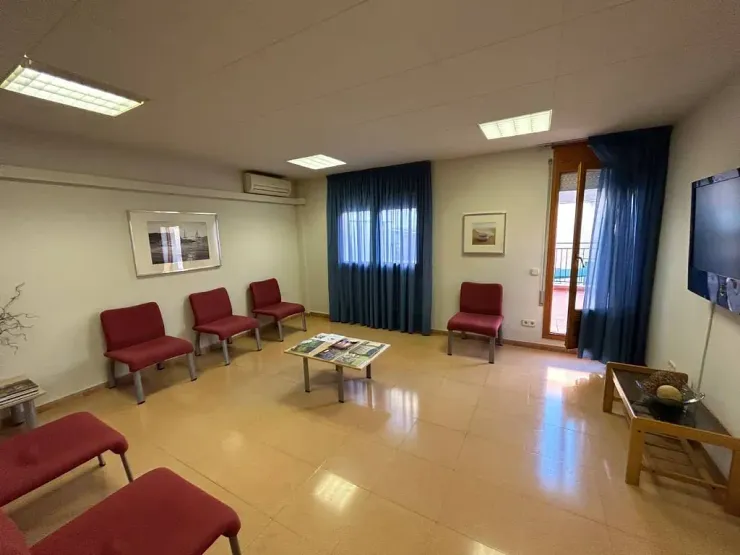 Una sala de espera con sillas rojas, una mesa y un televisor.