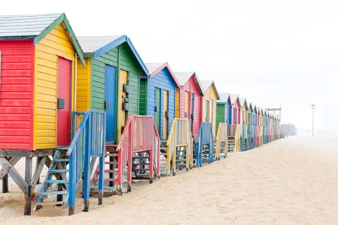 A row of colorful beach huts on a sandy beach in Muizenberg, Cape Town