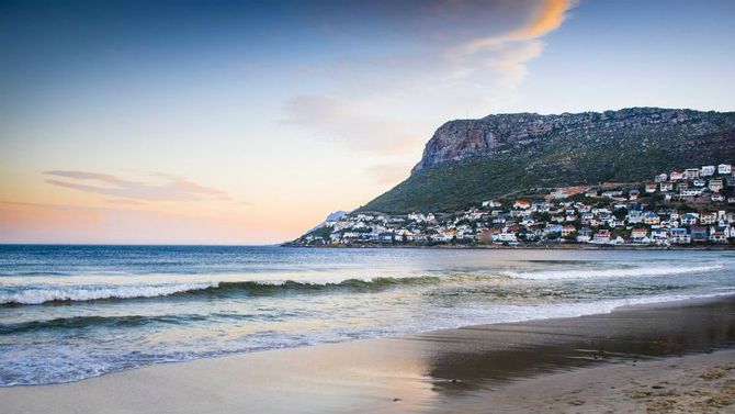 Fish Hoek beach with a mountain in the background and a city in the distance in Cape Town, Fish Hoek, Muizenberg, South Africa.