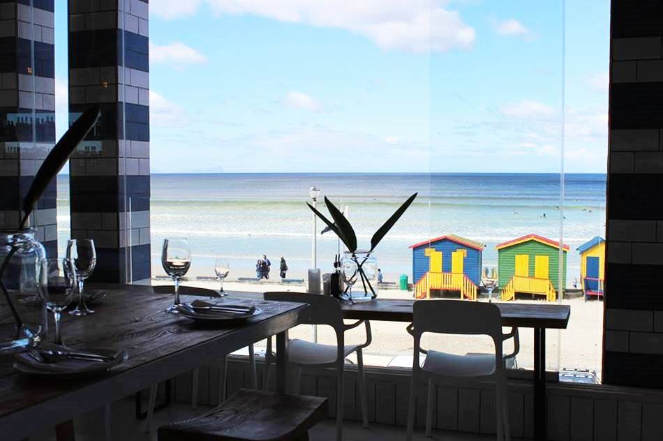 Row of colourful Muizenberg beach huts on the sand, symbolising strong community value, local identity, and visitor attraction.