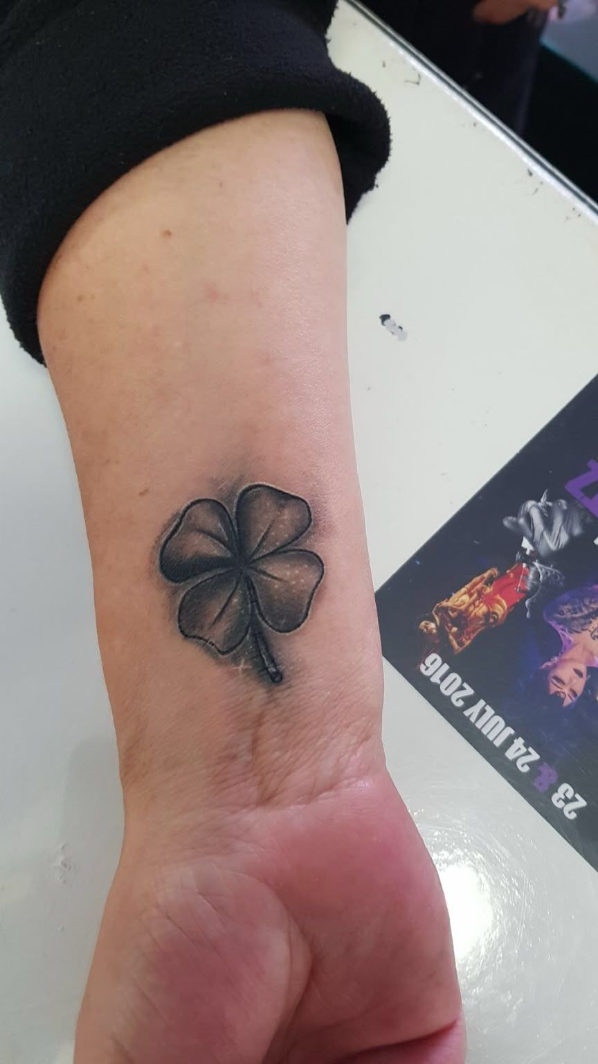 Antebrazo y muñeca con un tatuaje de un trébol de cuatro hojas negro cerca de la muñeca.