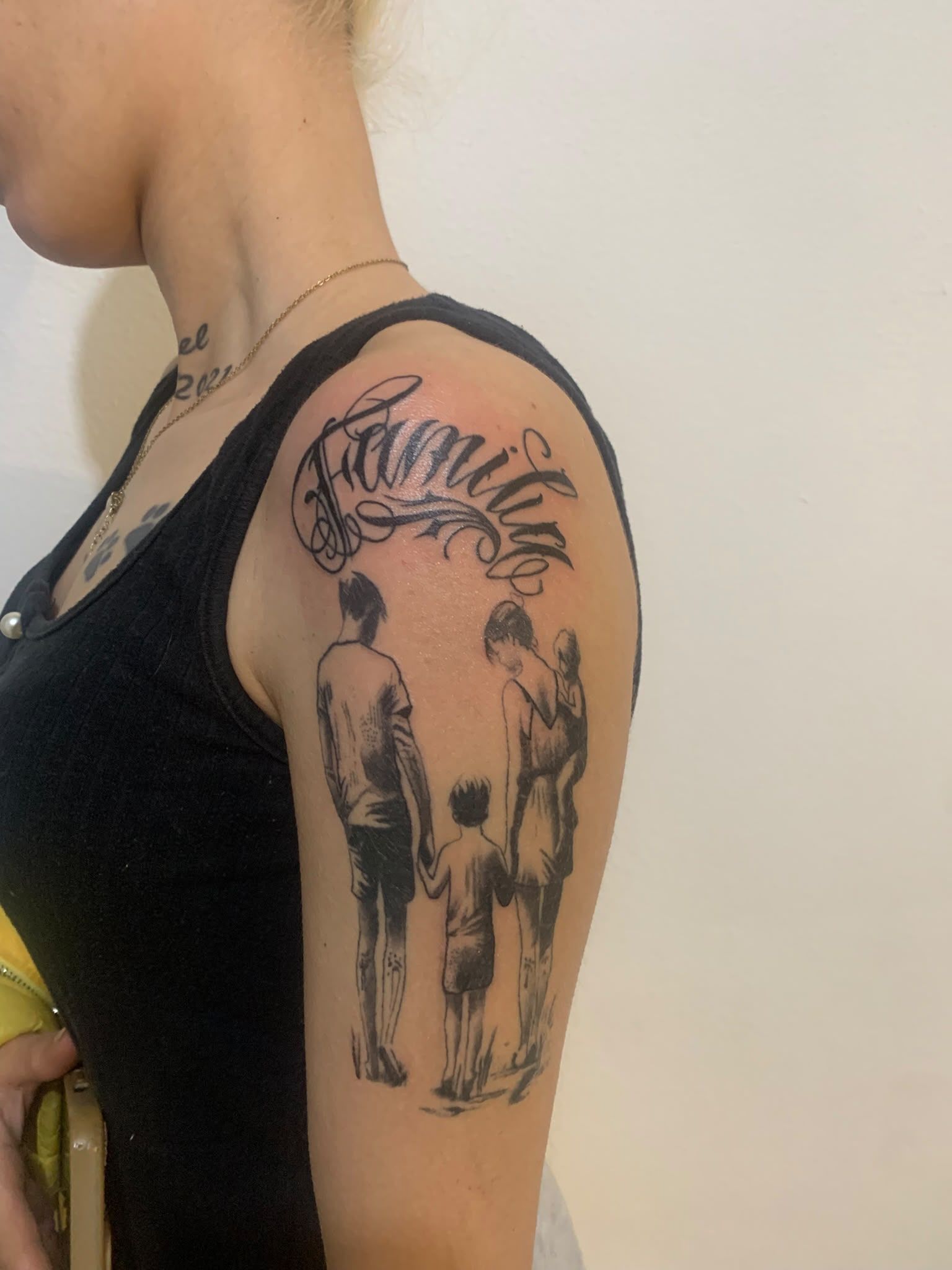 Persona con una camiseta negra de tirantes que muestra un tatuaje de un tigre y unas figuras colgantes en la parte superior del brazo