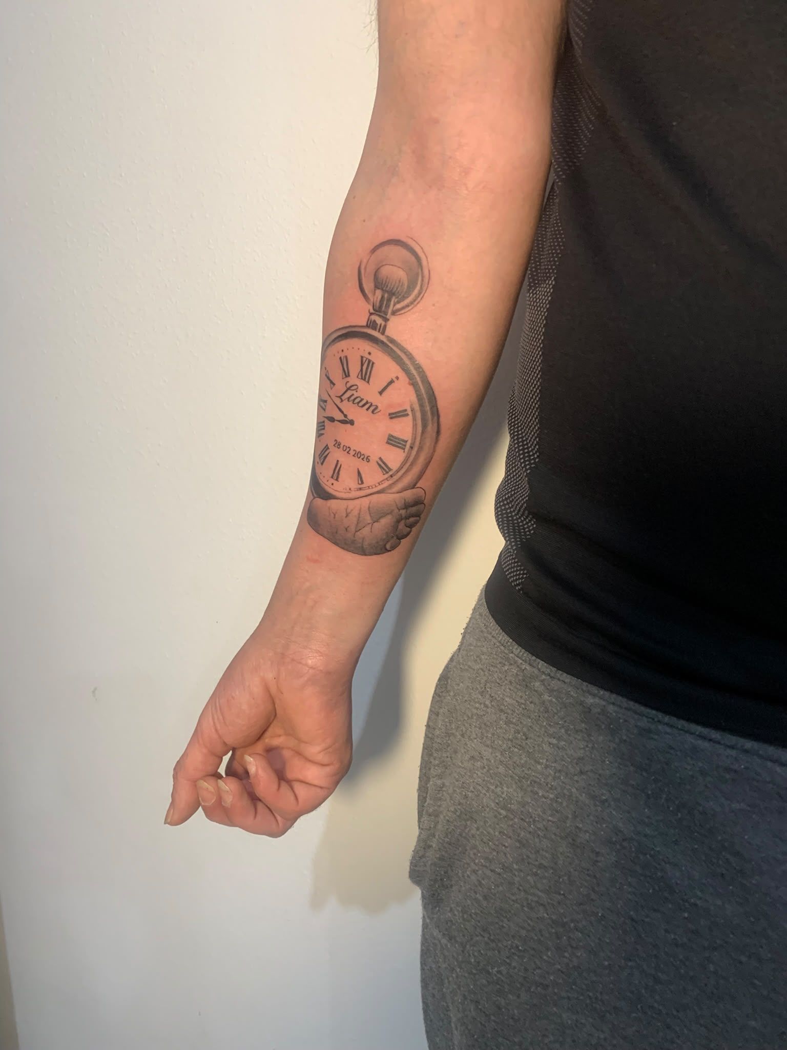 Primer plano de un antebrazo con un gran tatuaje de un reloj negro, con el brazo colgando a un lado.