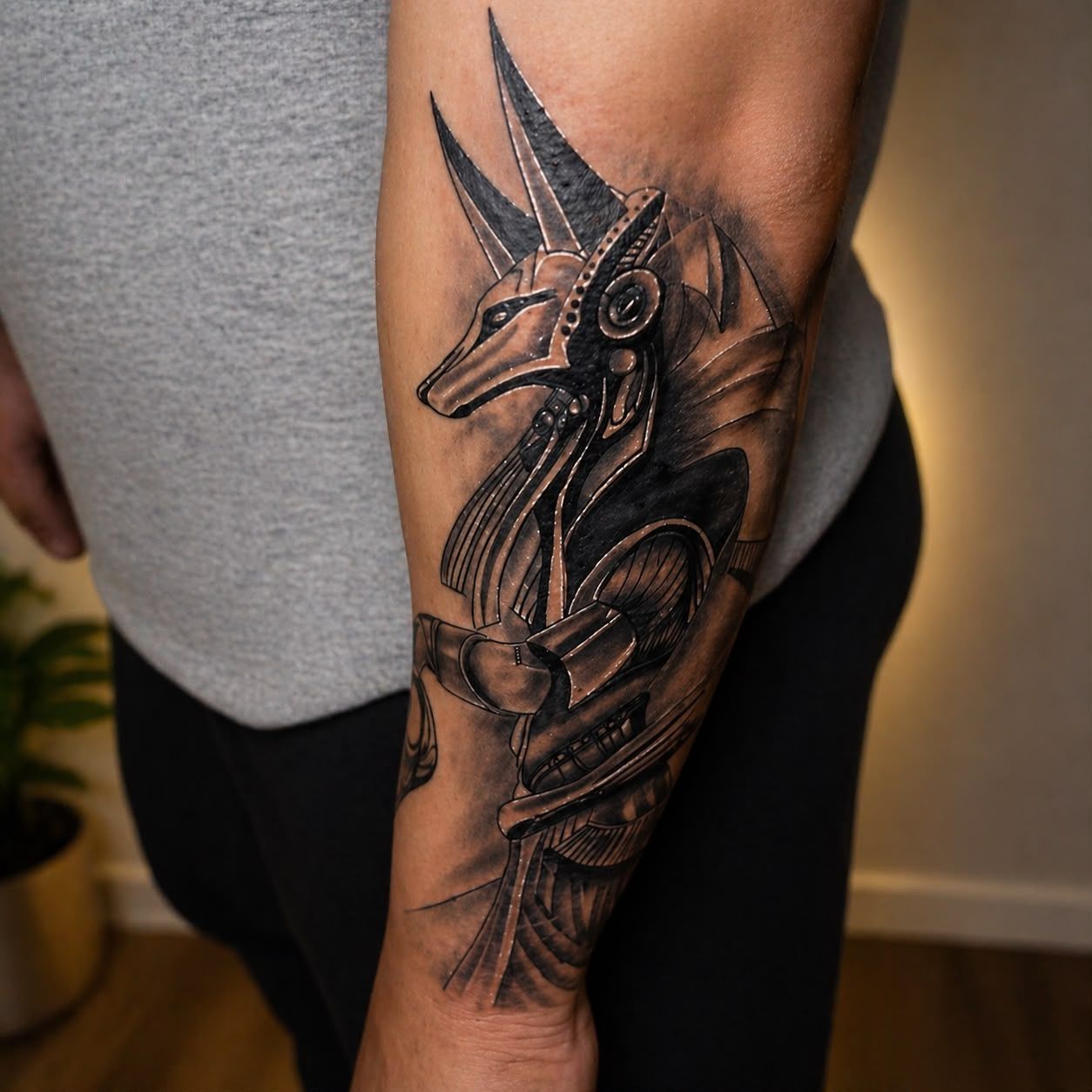 Tatuaje en negro y gris de Anubis en un antebrazo, que muestra a una figura egipcia con cabeza de chacal