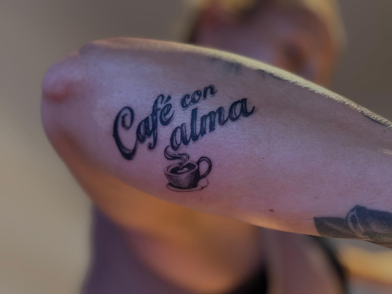 Tatuaje con la frase «Café con alma» y una pequeña taza de café en la planta del pie