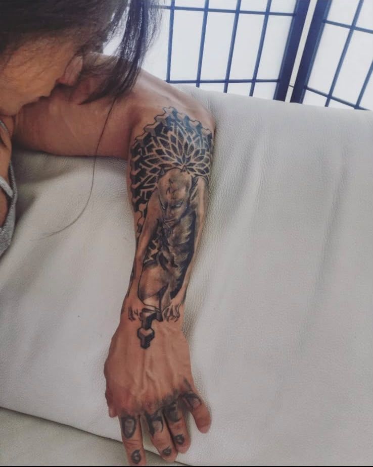 Antebrazo y mano tatuados apoyados sobre una manta blanca junto a una ventana