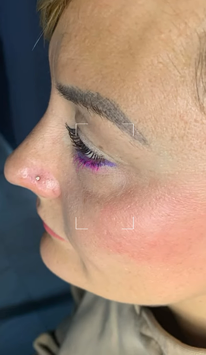 Perfil de una persona con maquillaje rosa en los ojos y un piercing en la nariz, sobre un fondo oscuro