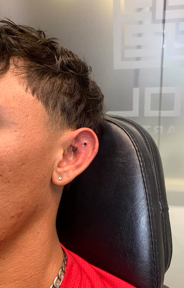 Perfil lateral de la oreja de una persona con un pequeño pendiente de aro, sentada frente a una silla negra y un fondo de vidrio esmerilado