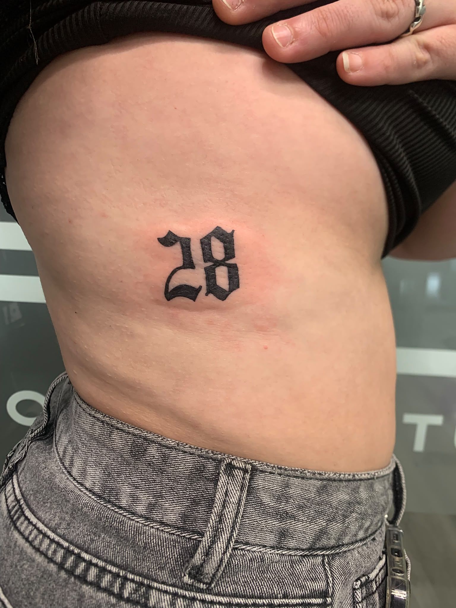 Primer plano del costado del torso, con un pequeño tatuaje negro con el número «28» cerca de la cintura.