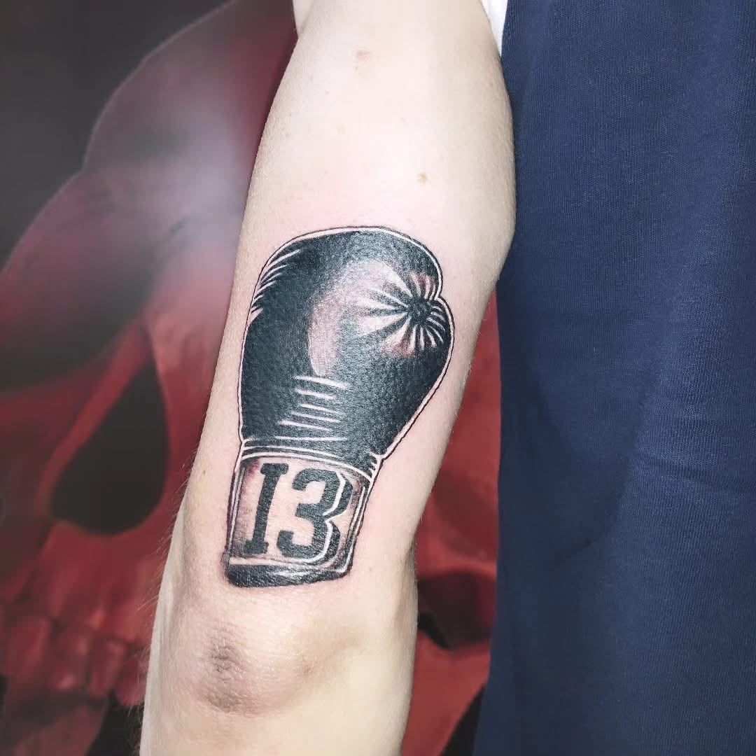 Tatuaje de un guante de boxeo negro con el número «13» en un brazo.