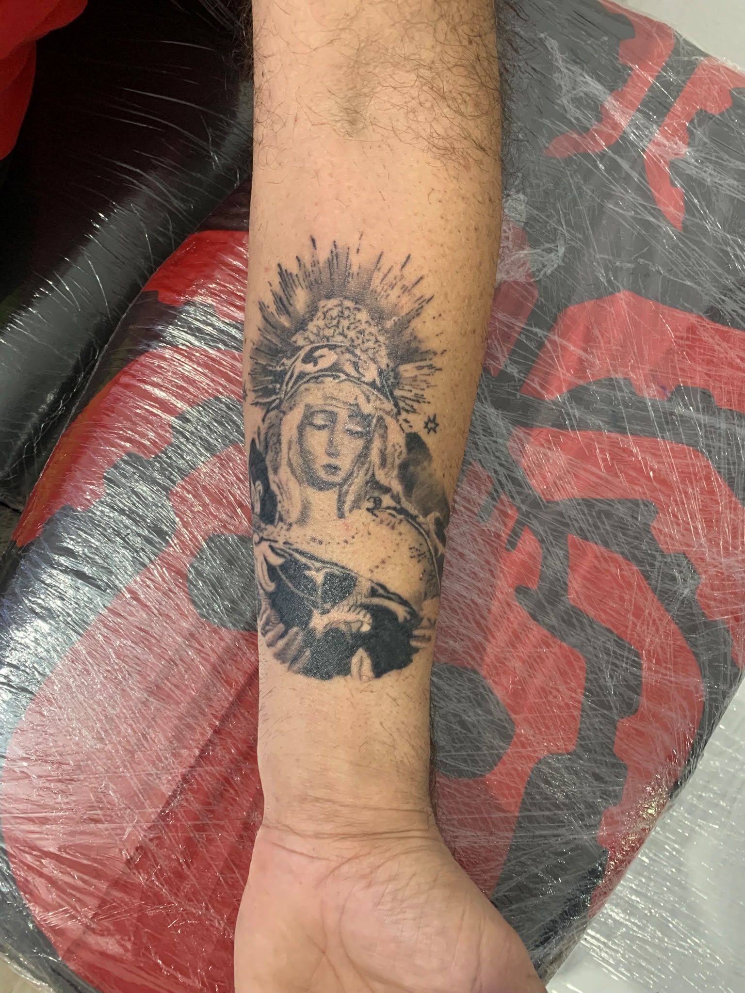 Antebrazo con un tatuaje negro de un rostro coronado o una figura religiosa por encima de la muñeca