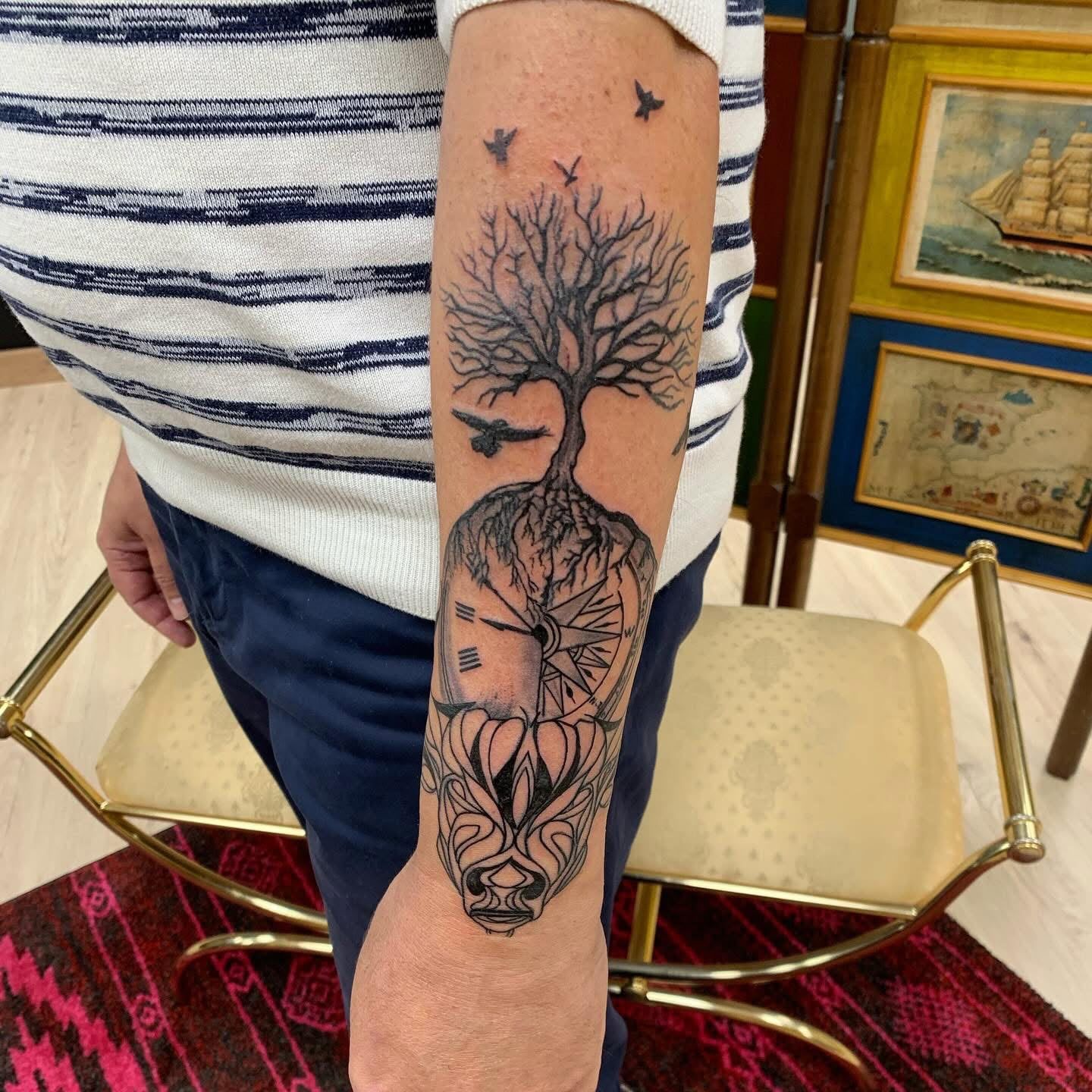 Brazo con un tatuaje negro de un árbol que crece de una cabeza humana, con estrellas y un barco enmarcados encima.