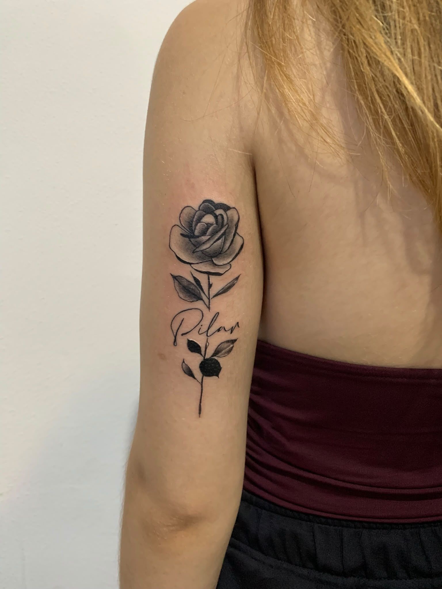 Brazo con un tatuaje floral negro en la parte superior, frente a una pared beige.