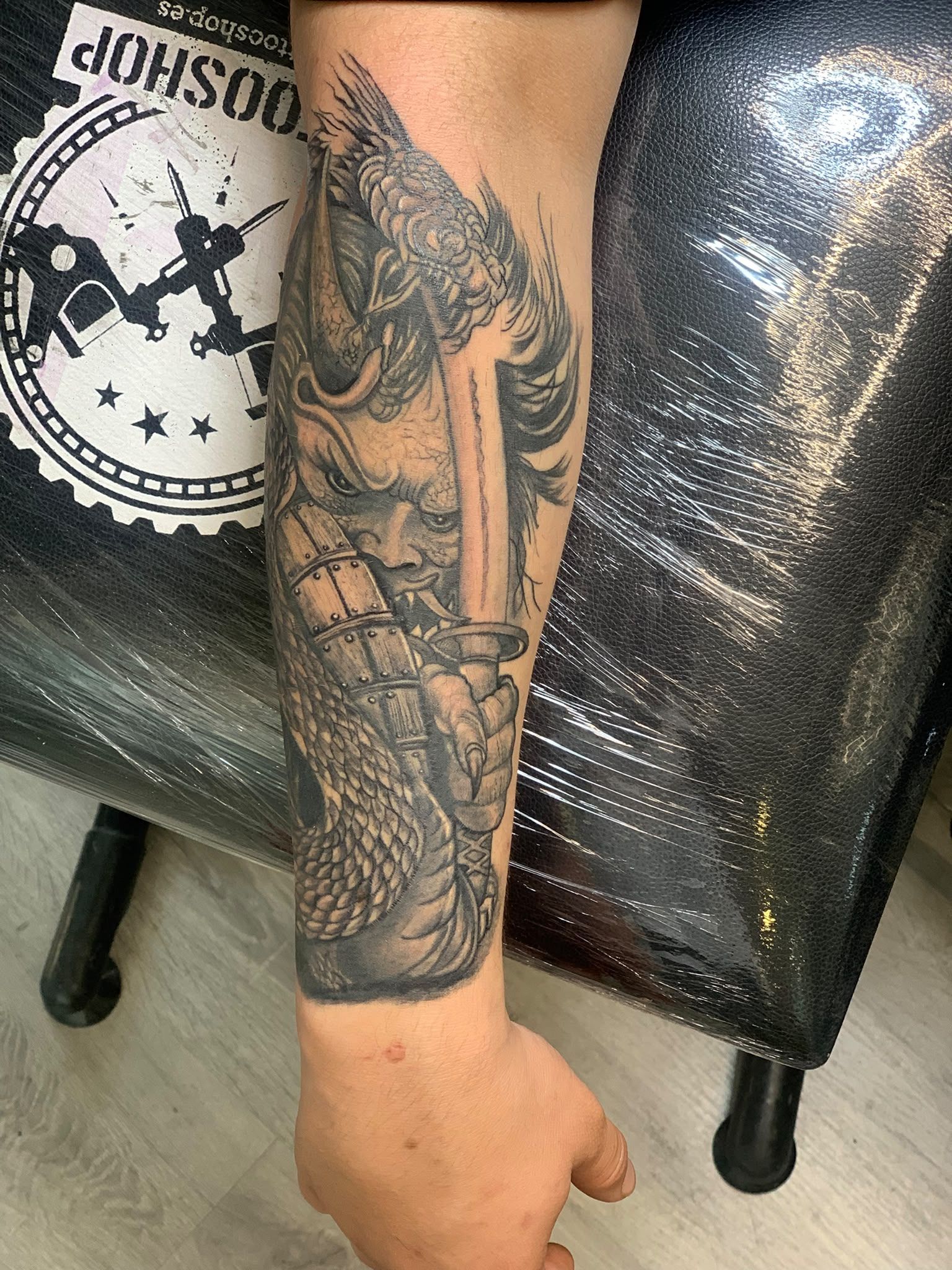 Antebrazo tatuado apoyado junto a una silla negra, con una camisa estampada y un tatuaje de elefante a la vista