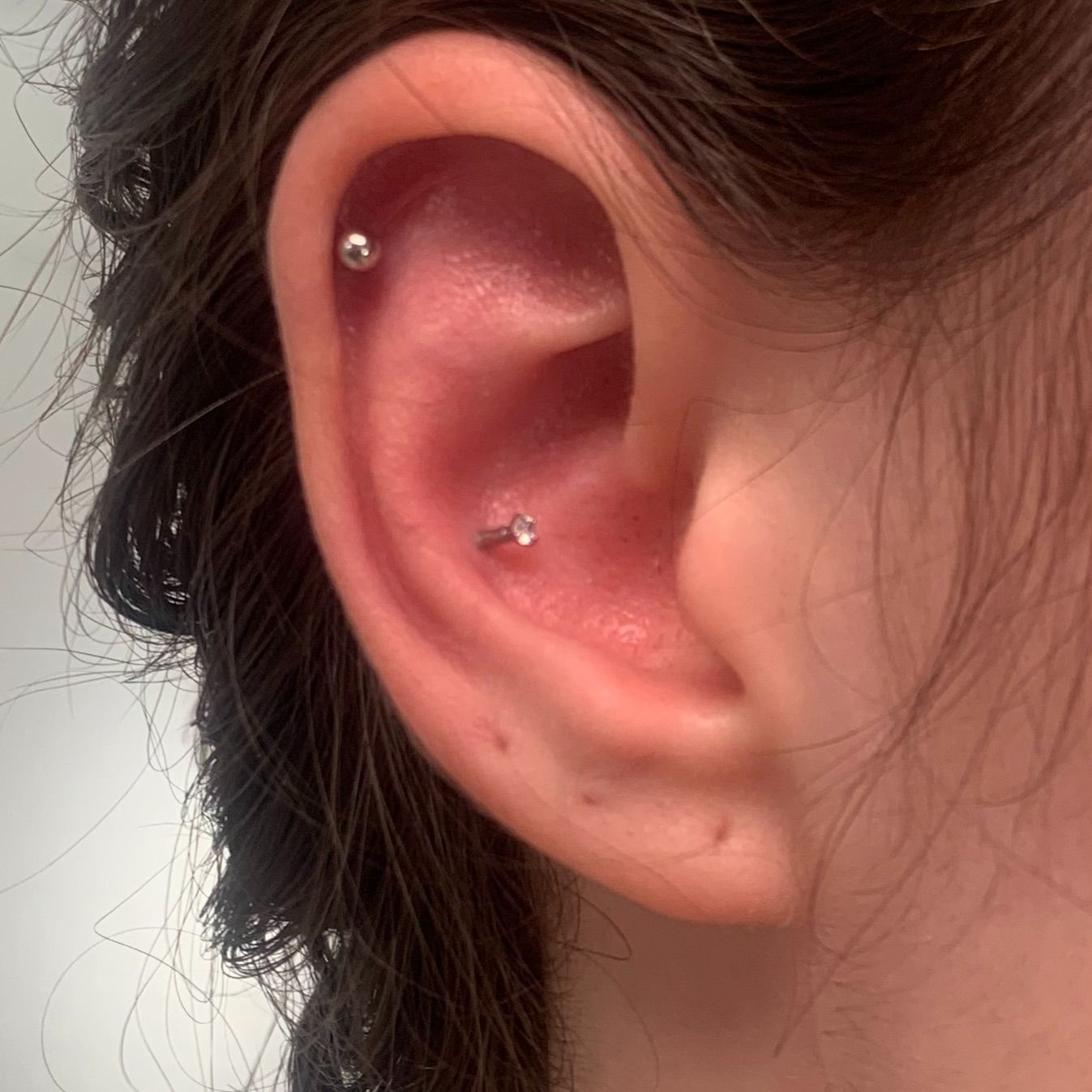 Primer plano de una oreja con dos piercings plateados, incluido un aro en el lóbulo inferior.