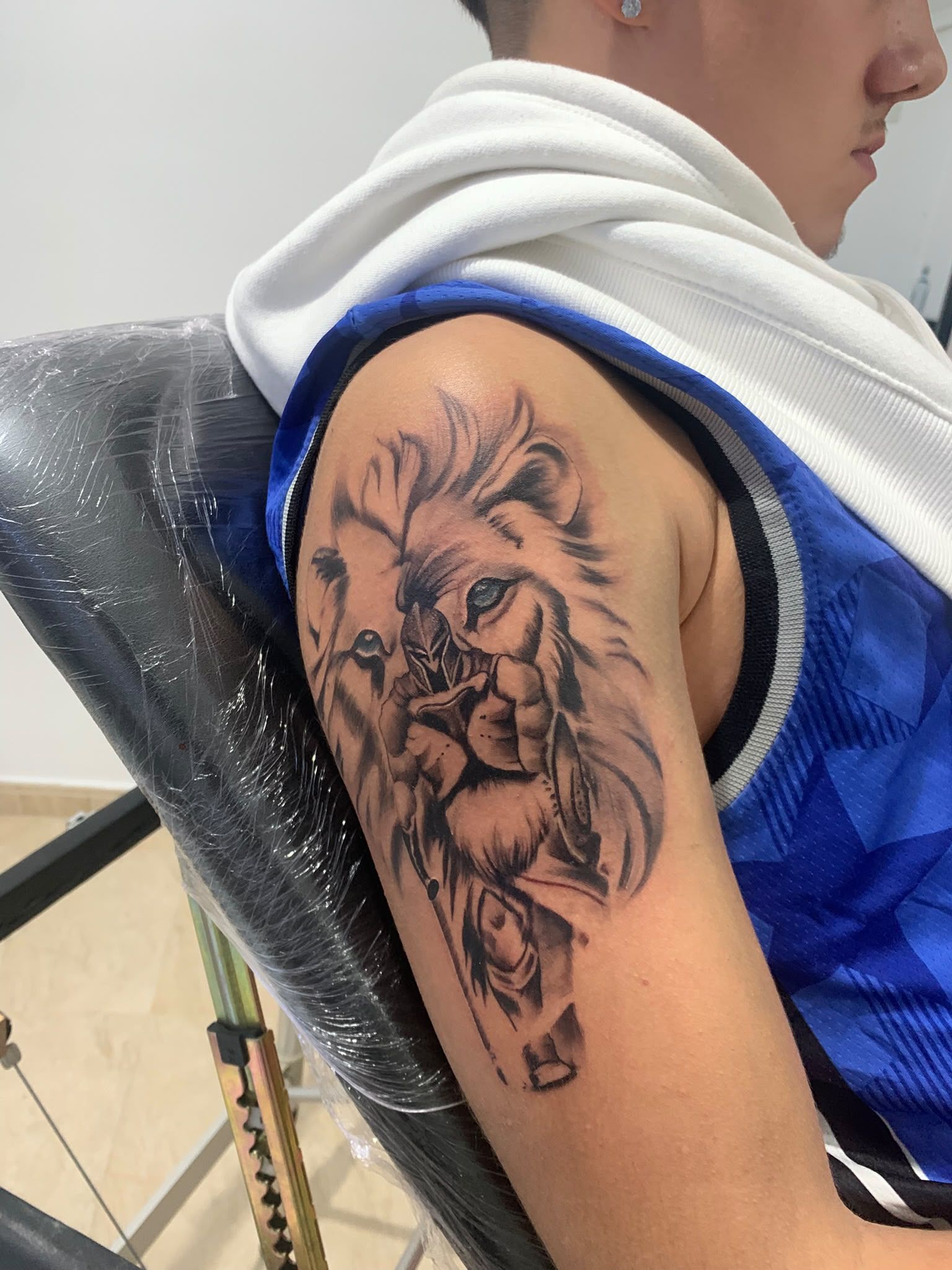 Tatuaje de león en la parte superior del brazo, con una camiseta sin mangas azul y una toalla blanca, en un gimnasio.