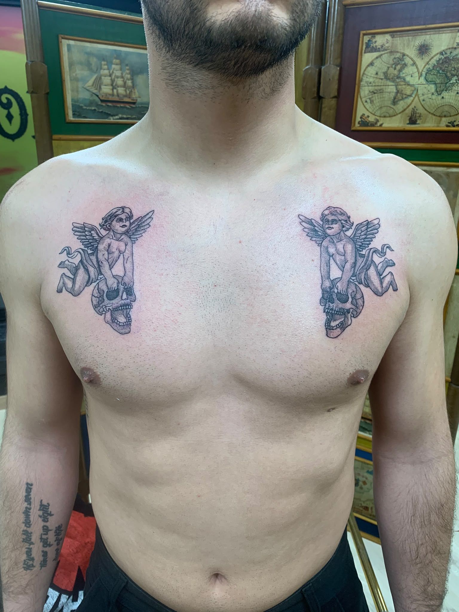 Torso de una persona sin camiseta, con tatuajes simétricos en el pecho, de pie en el interior, frente a unas paredes verdes.