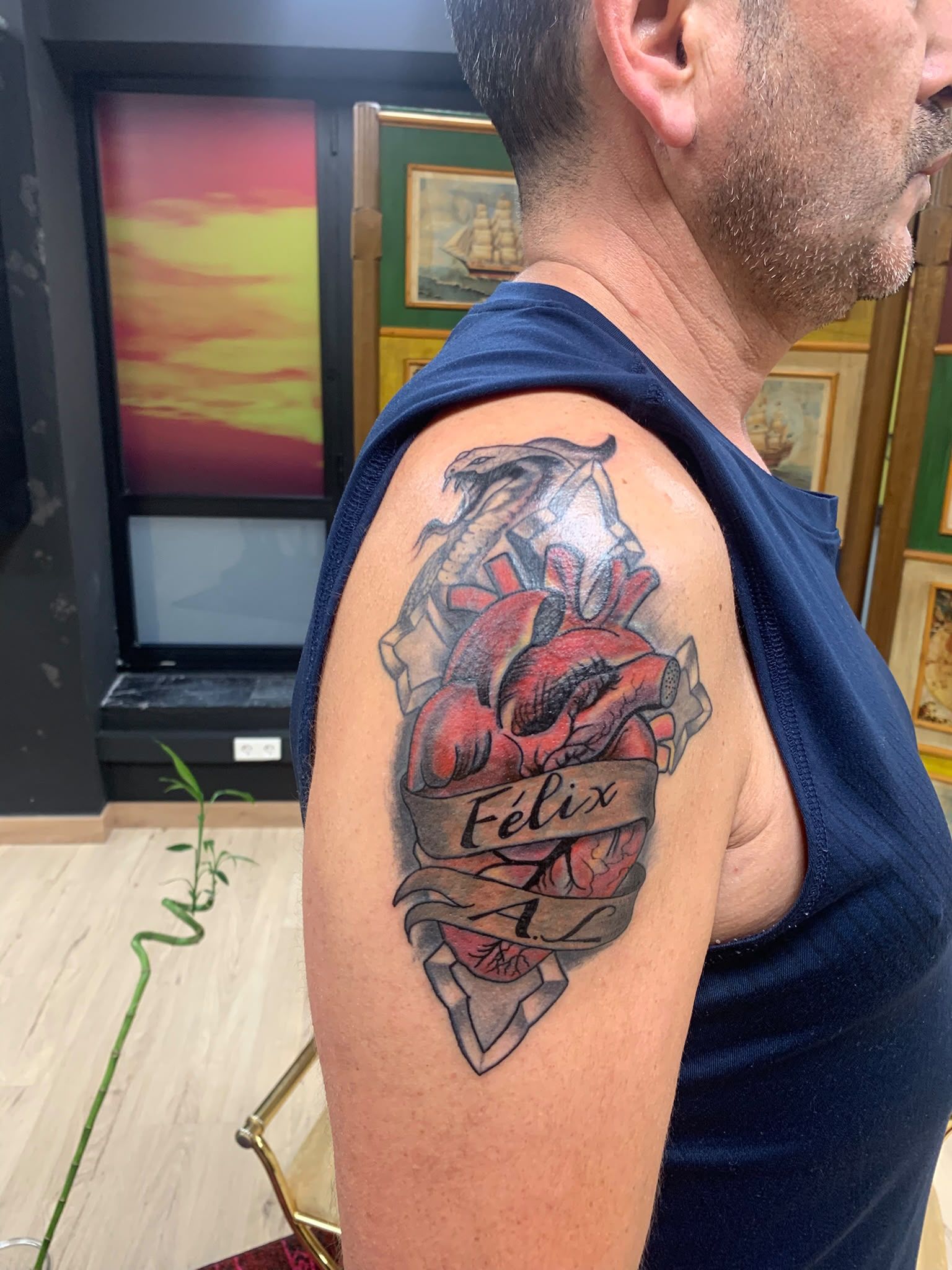 Vista lateral de una persona que muestra un colorido tatuaje en la parte superior del brazo, con rosas rojas y un texto en letra cursiva.