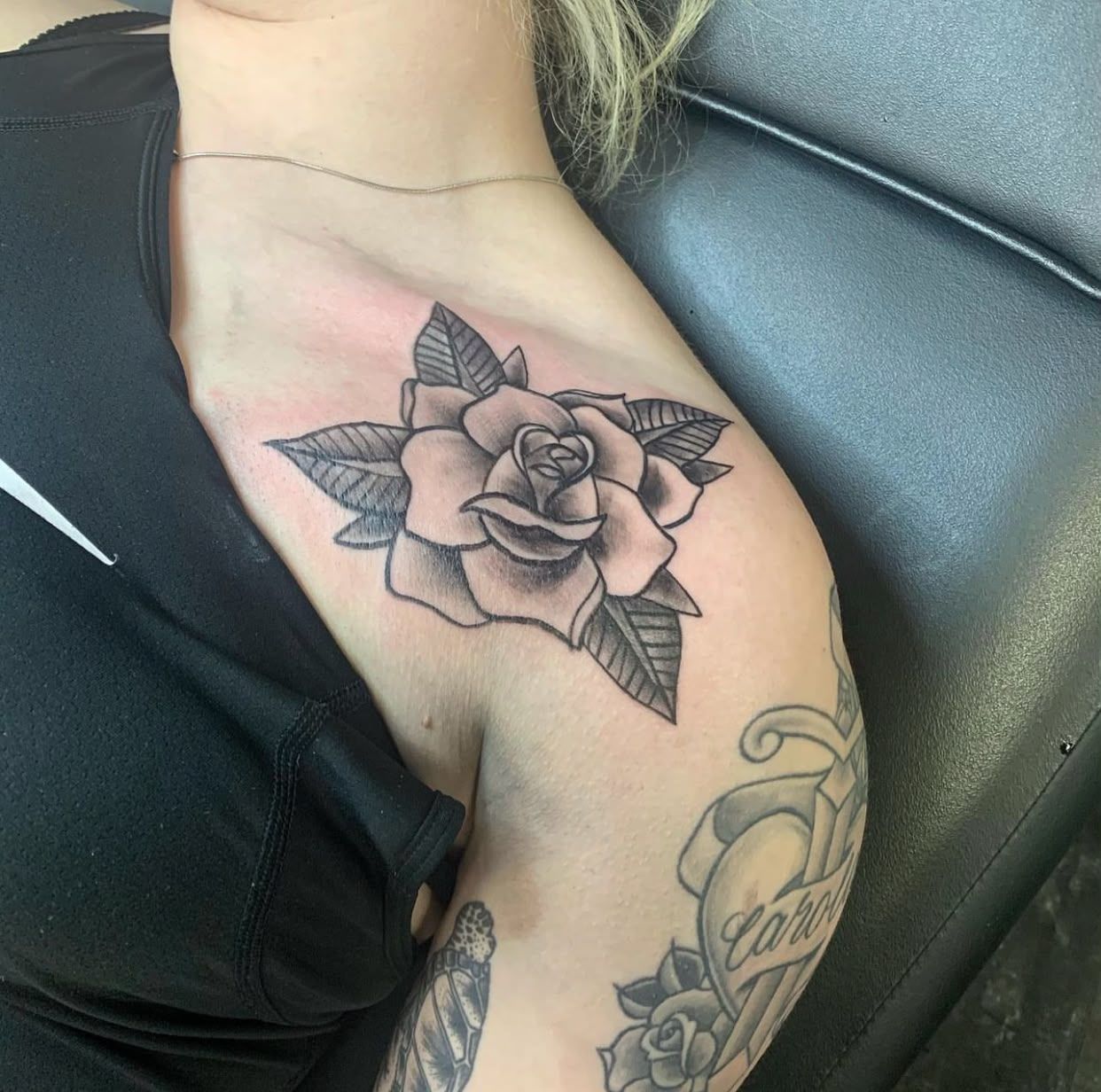 Tatuaje de una rosa en la parte superior del pecho de una persona, cerca del hombro, con trazos en negro y gris.