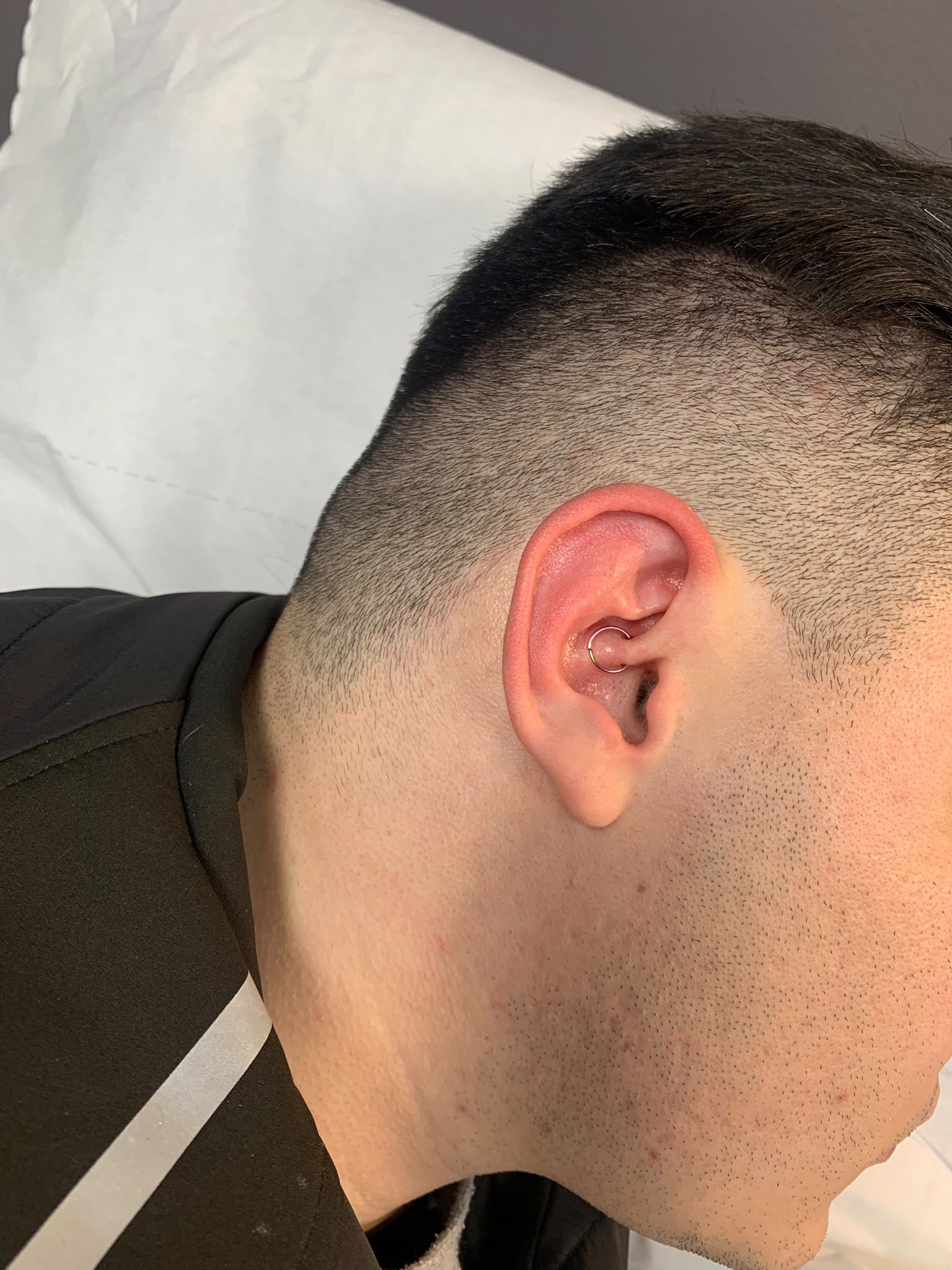 Perfil de una persona con un corte de pelo corto y degradado, con la oreja y el cuello visibles sobre una almohada blanca.