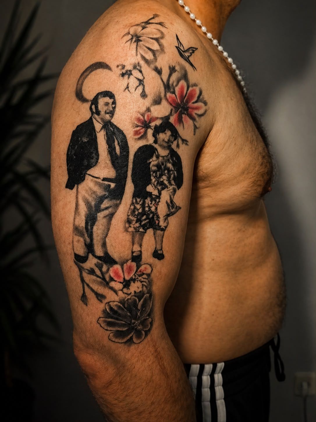 Tatuaje en la parte superior del brazo de dos personas con flores y pájaros en el hombro y el brazo de alguien