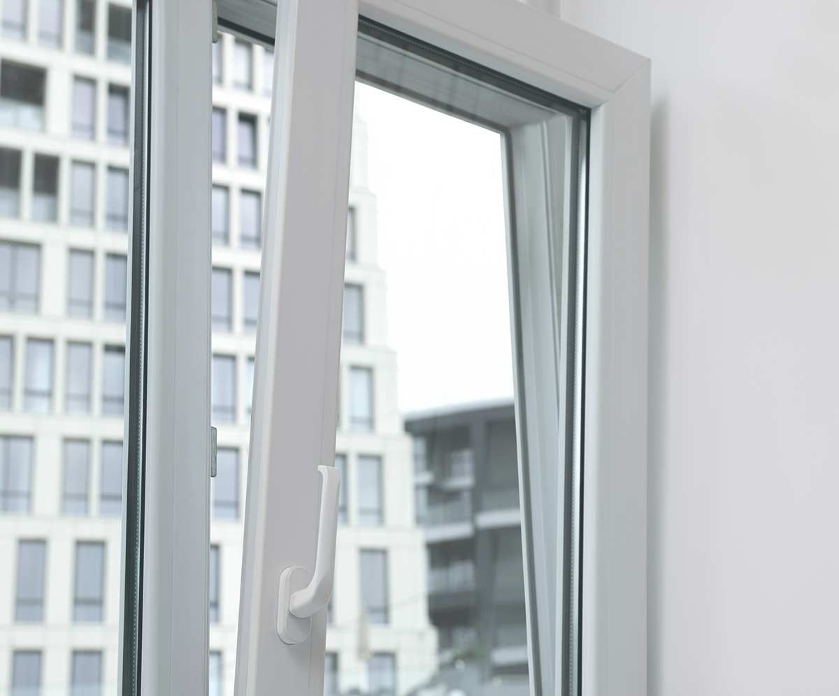 Ventana blanca parcialmente abierta, mostrando un edificio alto y un cielo brillante.