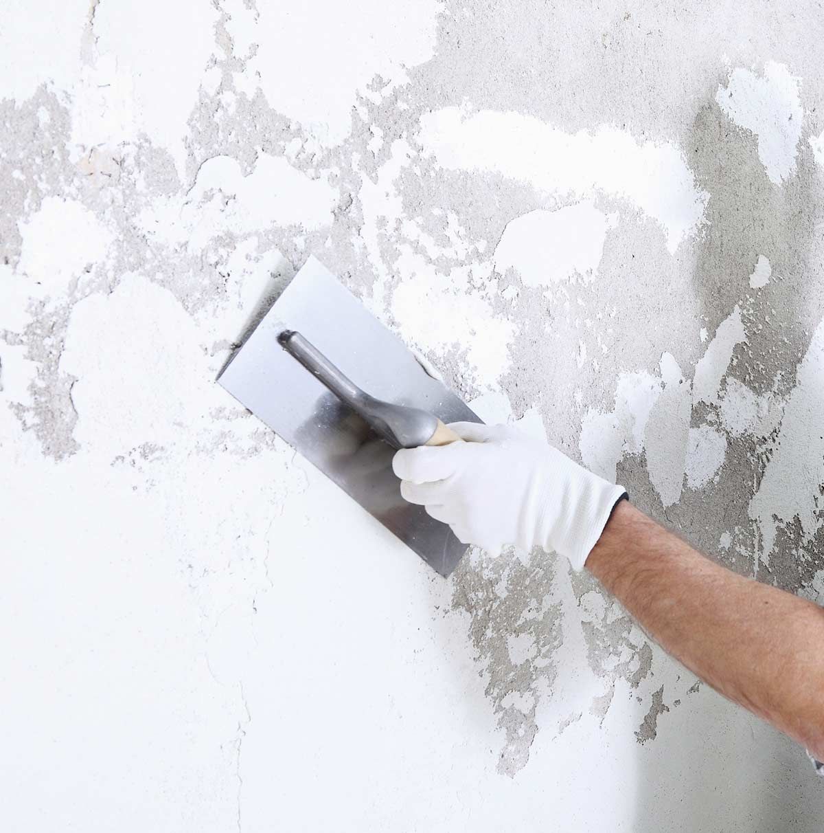 Mano con guante blanco utilizando una paleta para aplicar yeso a una pared.