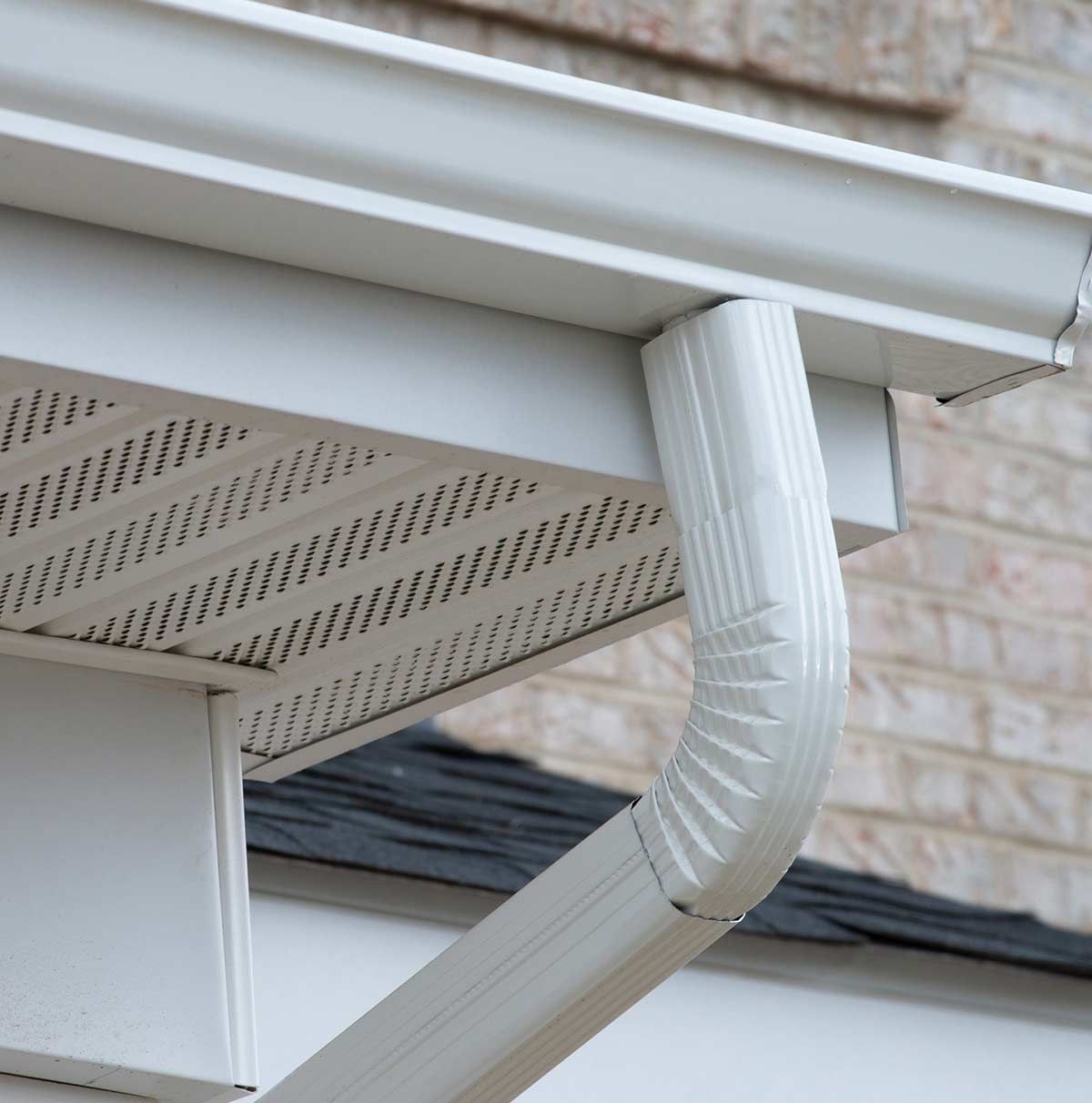Canalón y bajante de lluvia de color blanco en una casa con fachada de ladrillo.