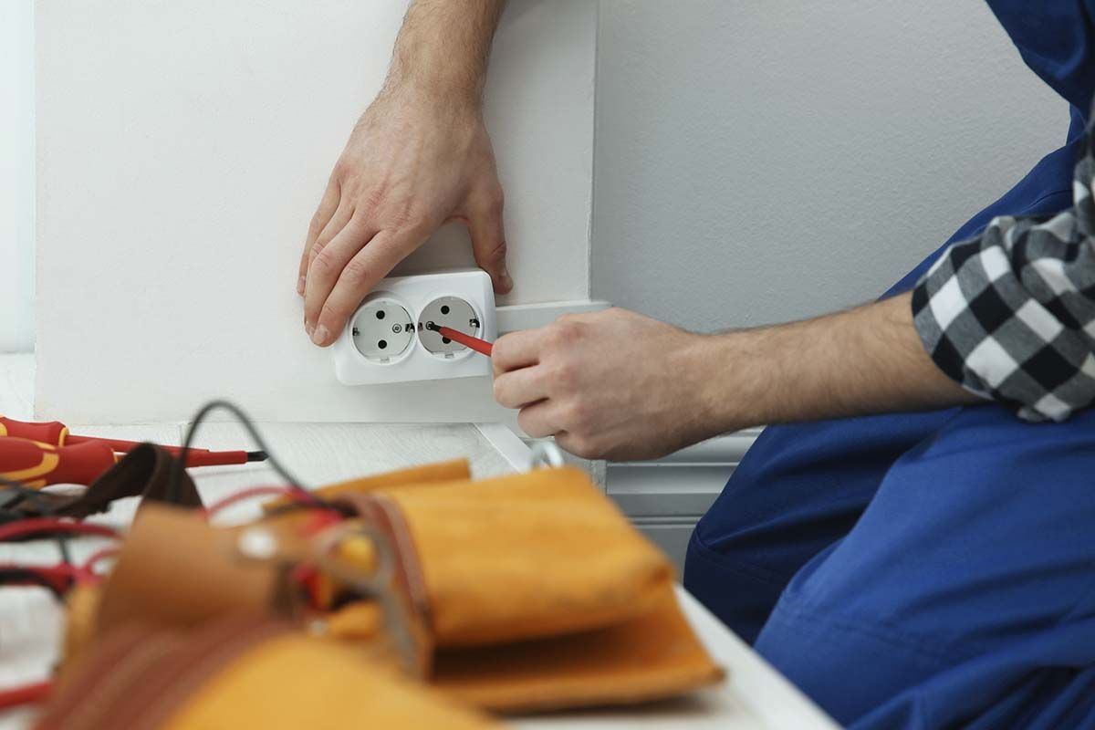Electricista instalando un enchufe europeo. Con overol azul y un destornillador.