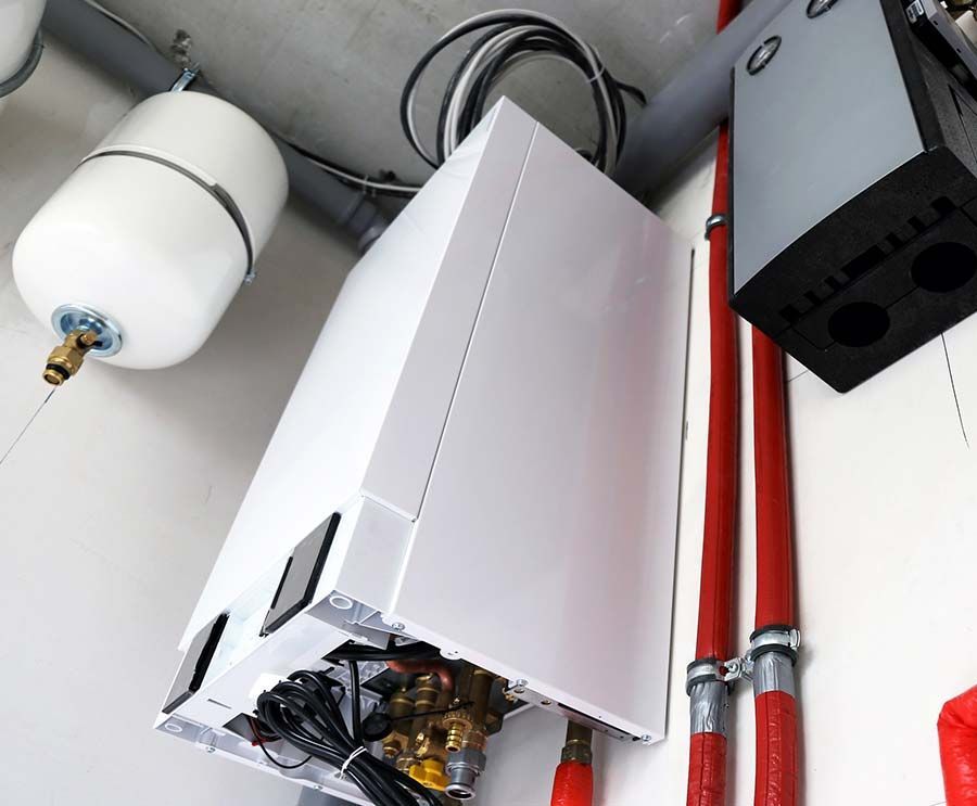 Caldera blanca y vaso de expansión en pared con tubos rojos y cables negros.
