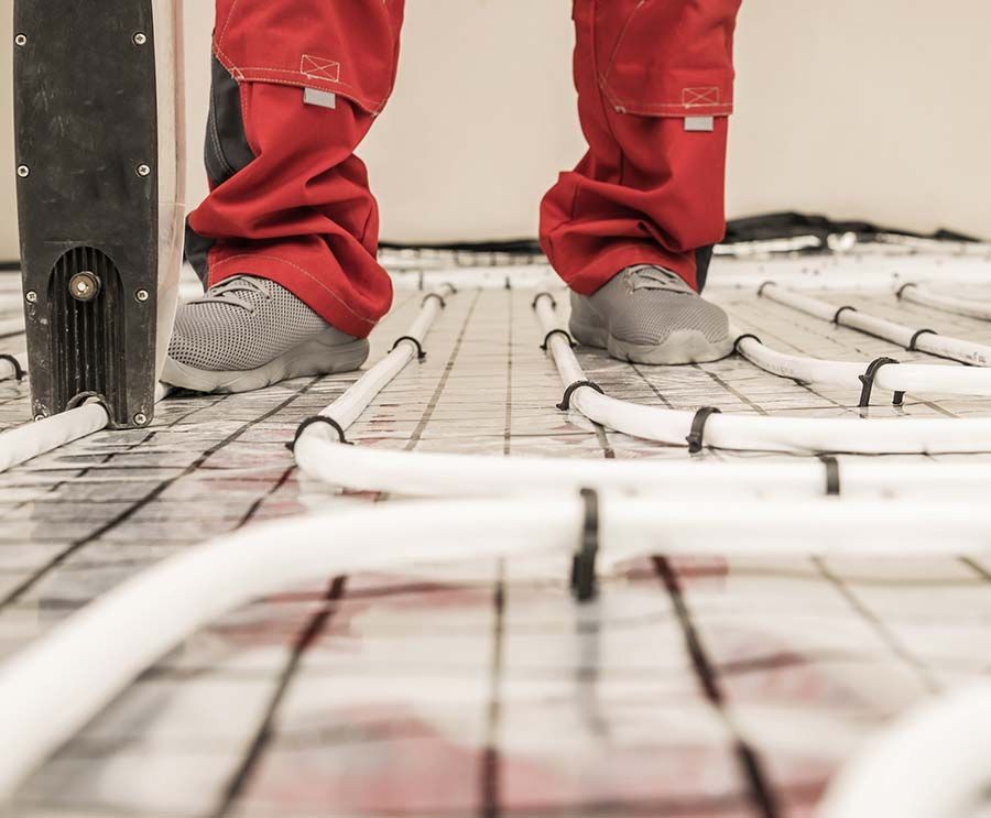 Persona con pantalones rojos instalando un sistema de calefacción por suelo radiante con tuberías blancas.