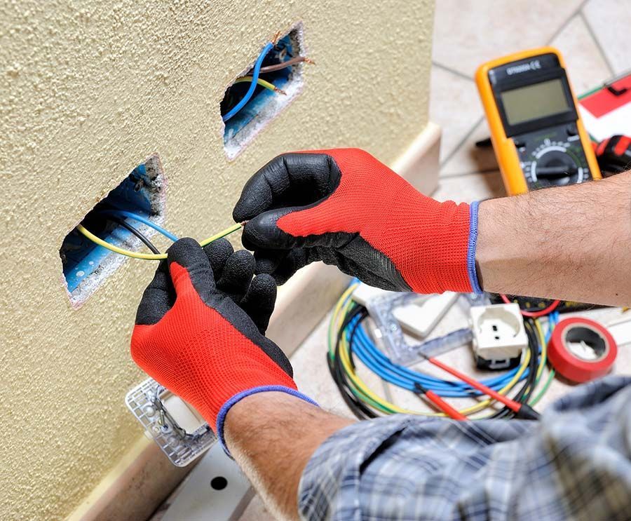 Persona con guantes rojos conectando cables eléctricos a un tomacorriente de pared.