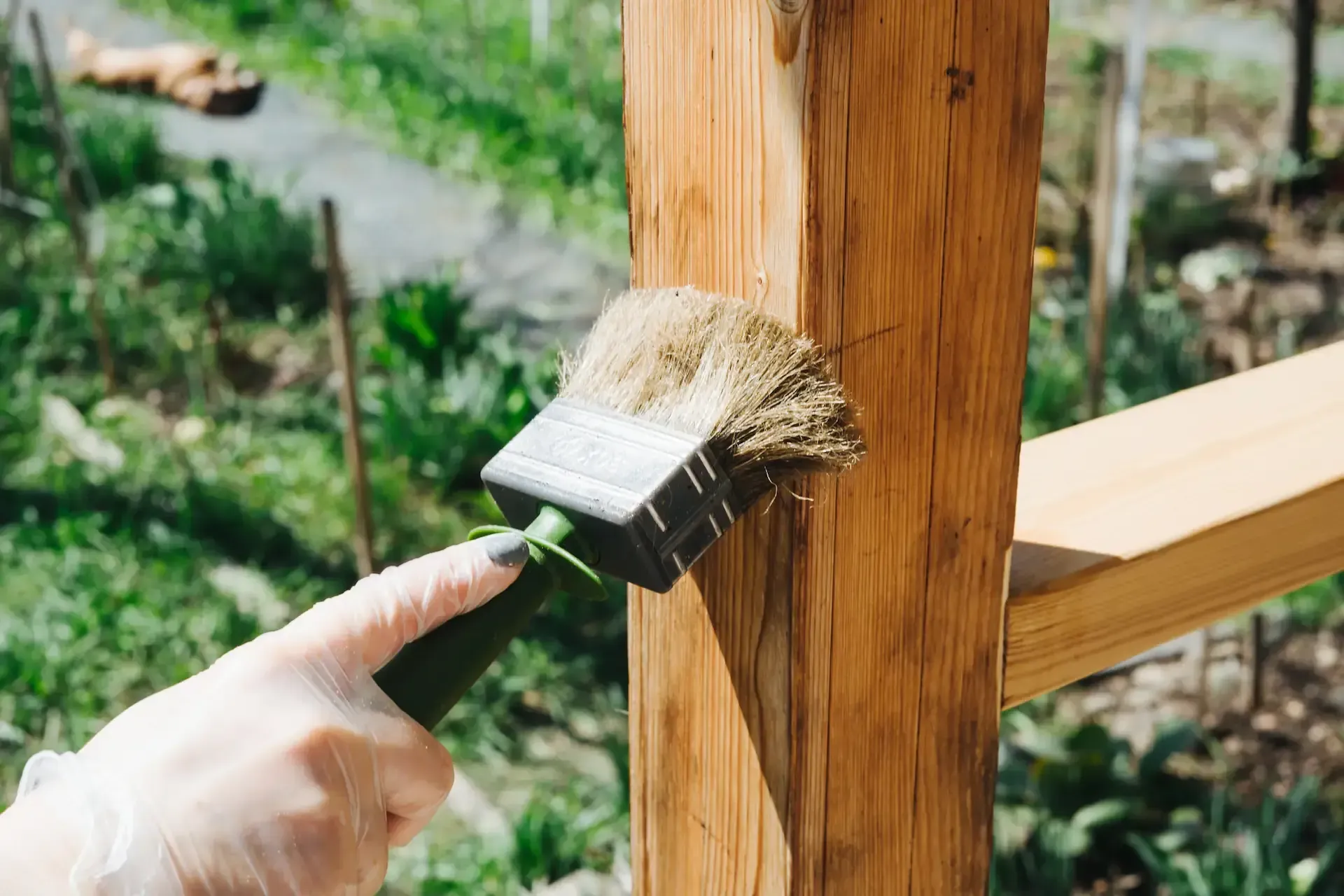 Mano con guante cepillando un poste de madera con un pincel al aire libre.